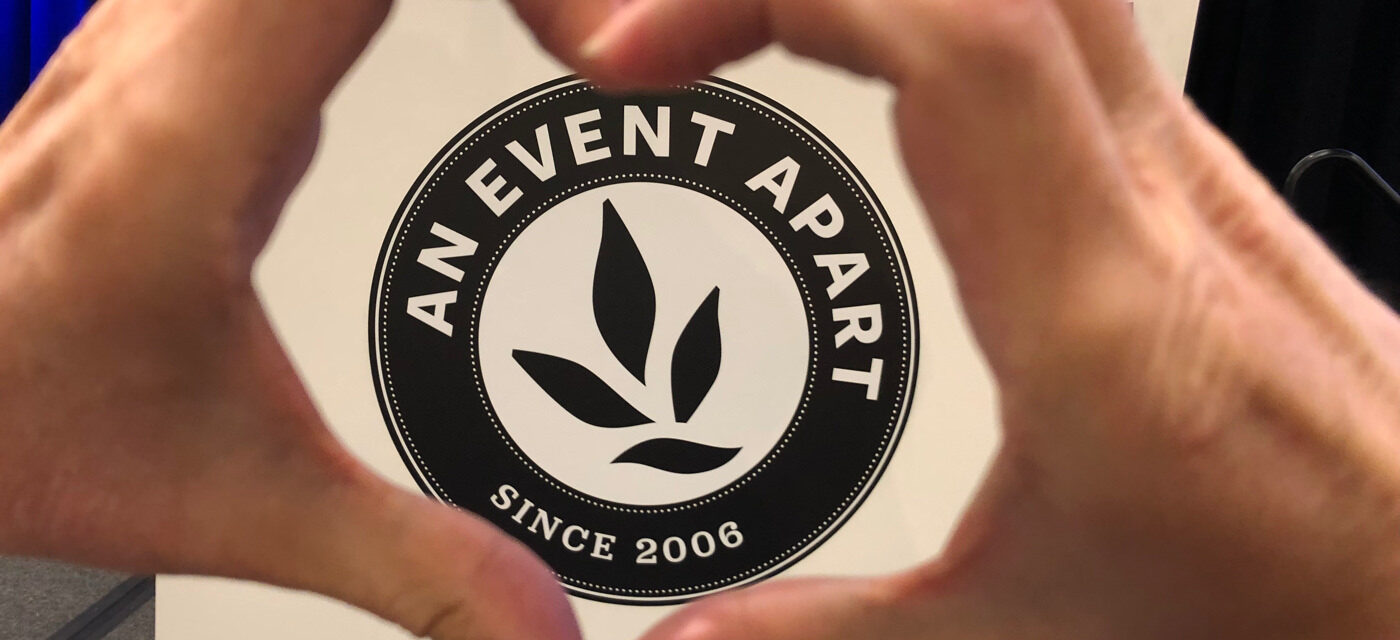 Two hands forming the shape of a heart around the An Event Apart logo