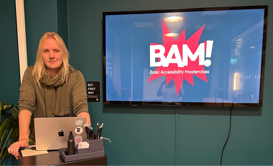 Alexander standing in front of a big TV screen with the text "BAM! Basic Accessibility Masterclass".